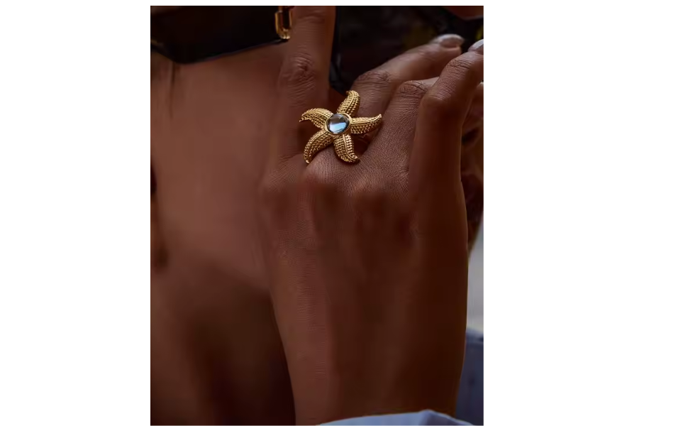 Gold ring with a starfish design and blue gemstone on a person's finger.